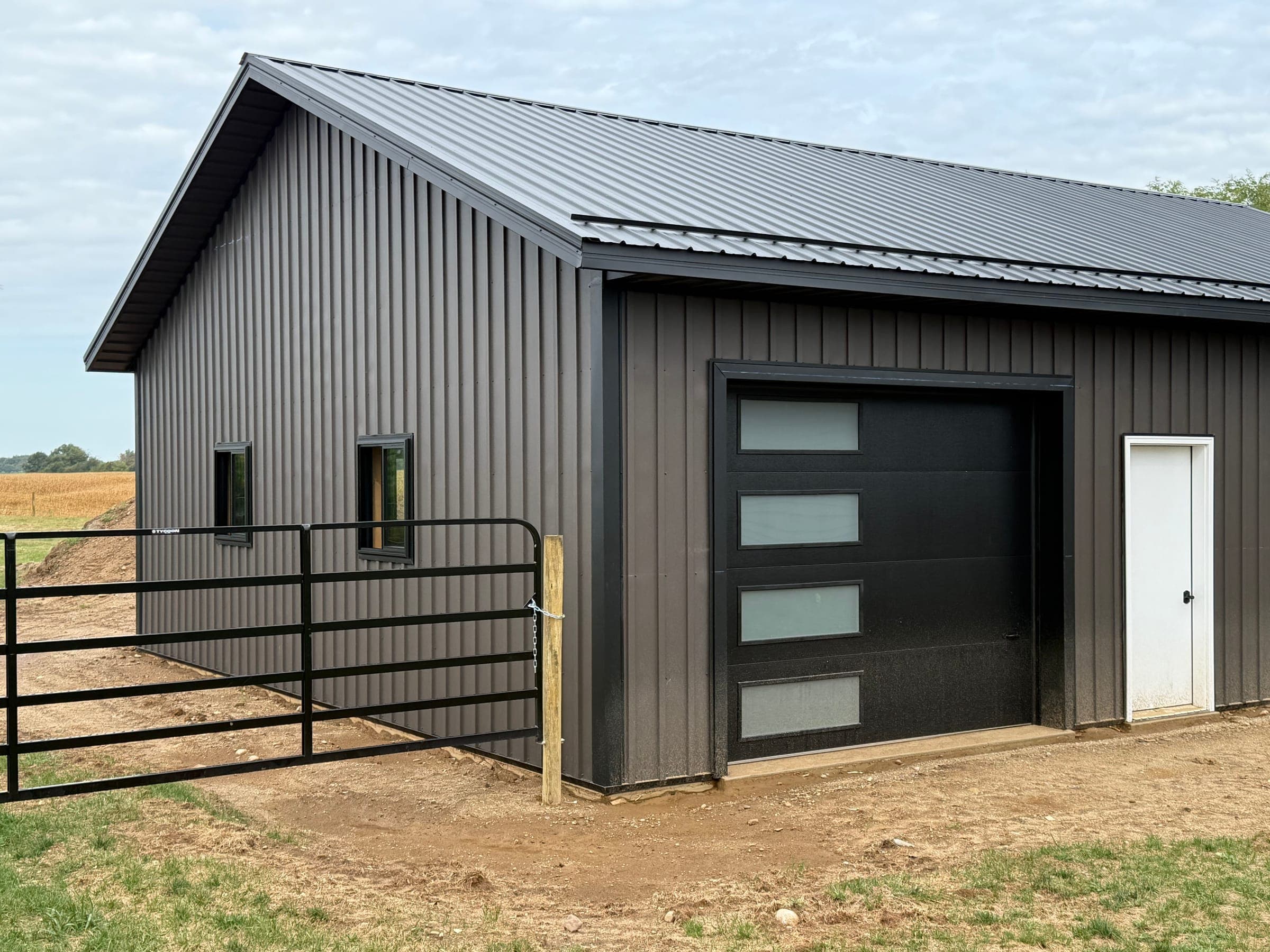 Corner view of modern dark post-frame barn with garage door and metal fencing in Indiana