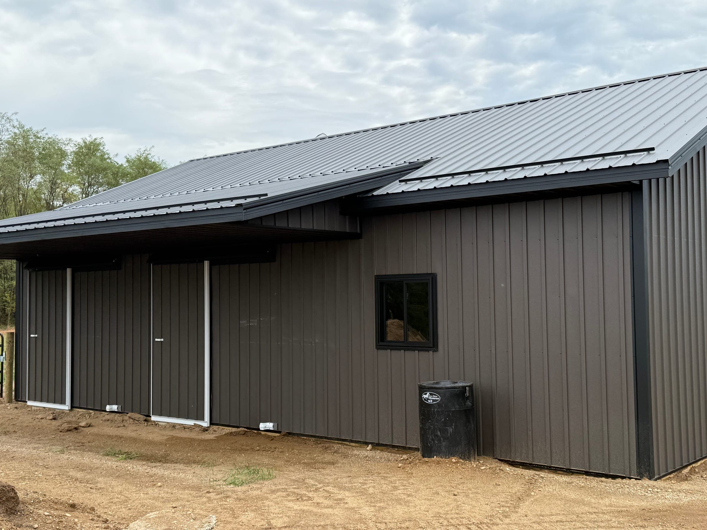 Rear view of dark charcoal post-frame barn showing roofline and steel cladding