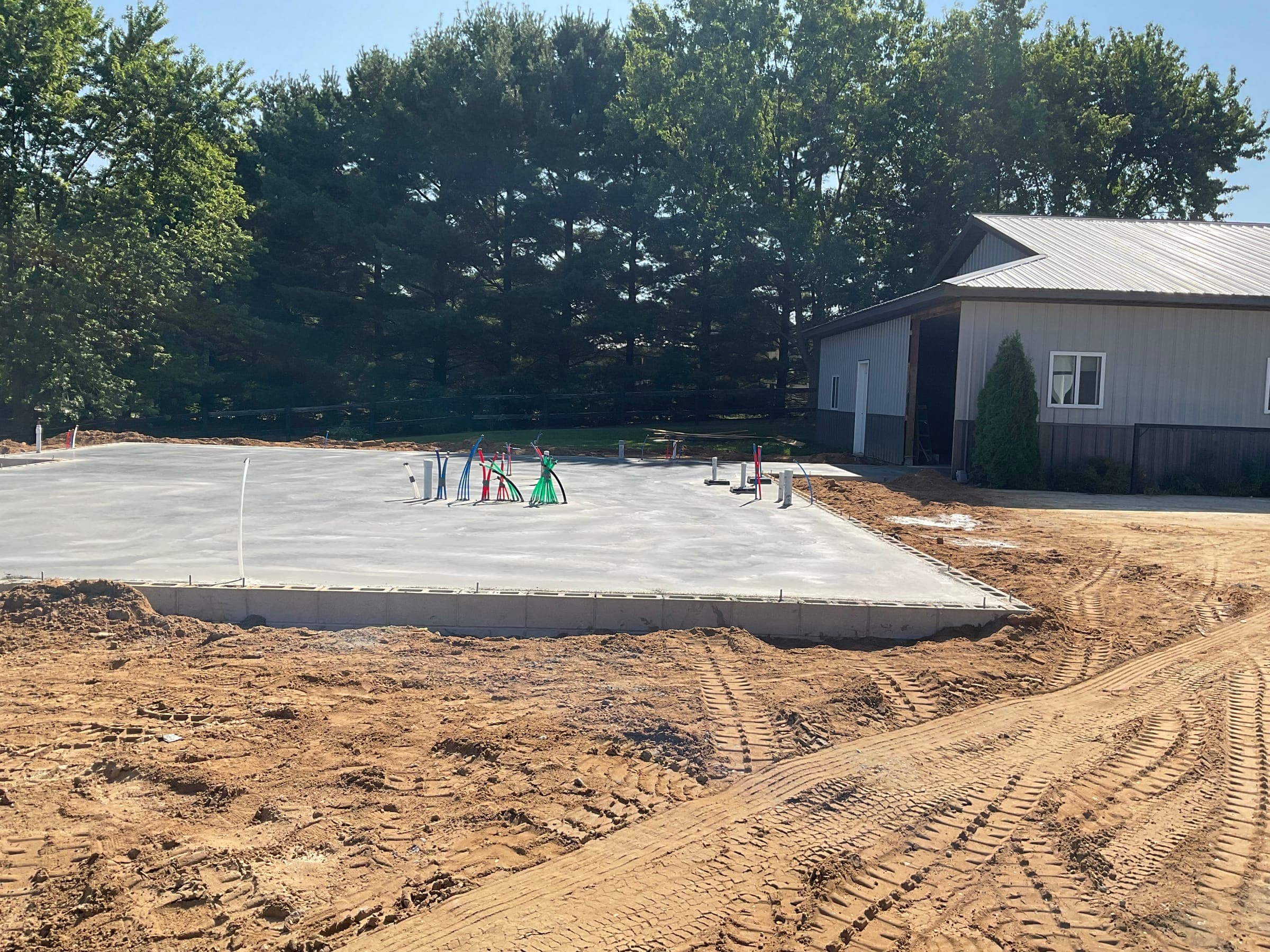Concrete foundation with plumbing stubs for residential build next to existing structure