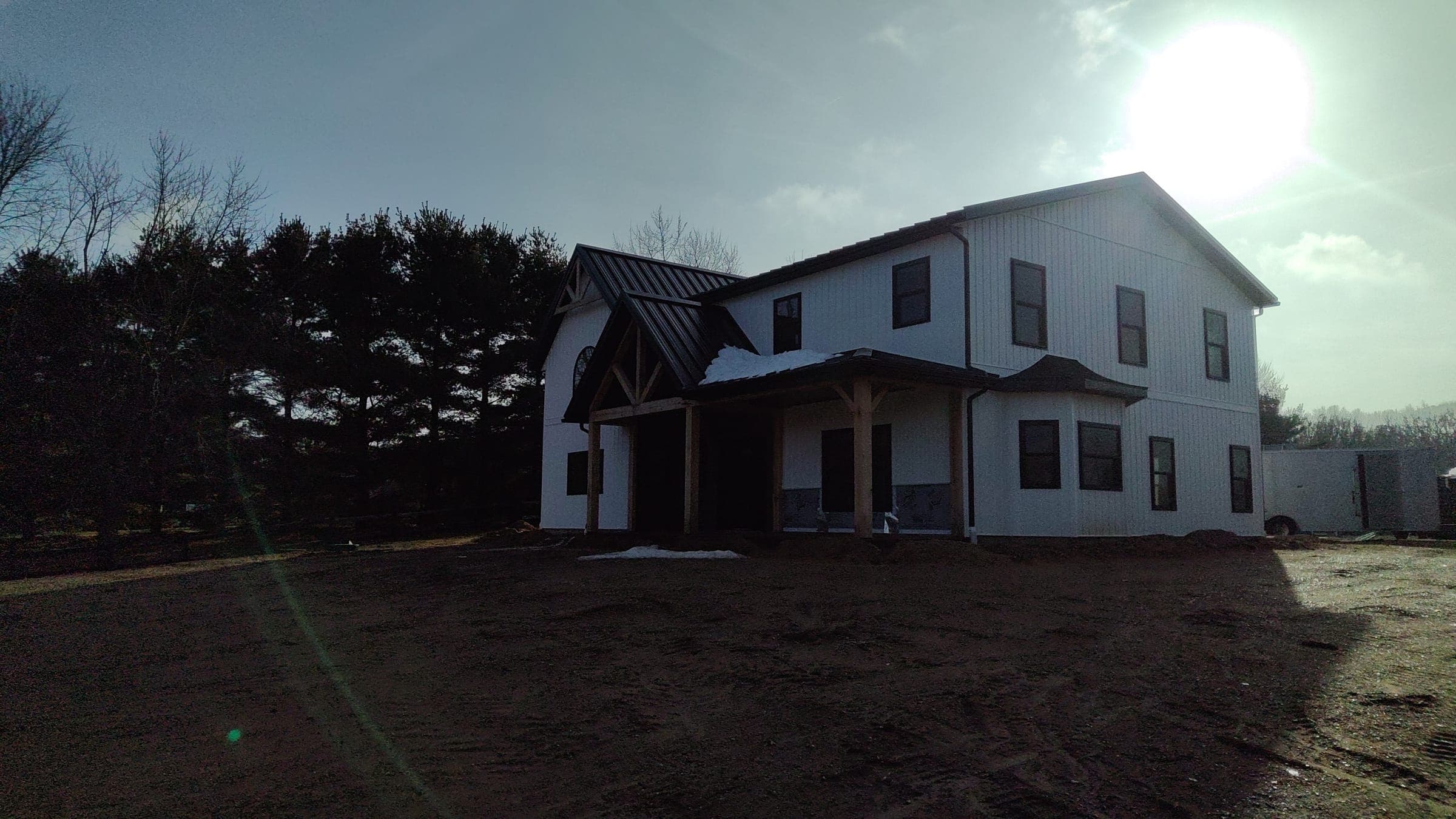 Custom farmhouse exterior backlit by afternoon sun showing full two-story profile