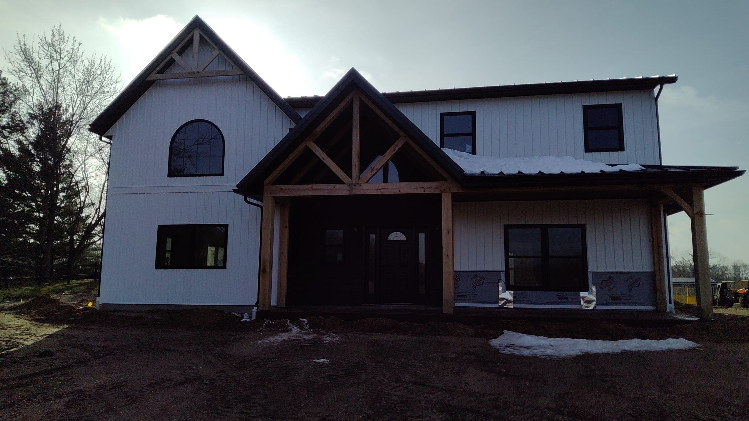 Front elevation of custom modern farmhouse with exposed timber trusses by Starlite Builders