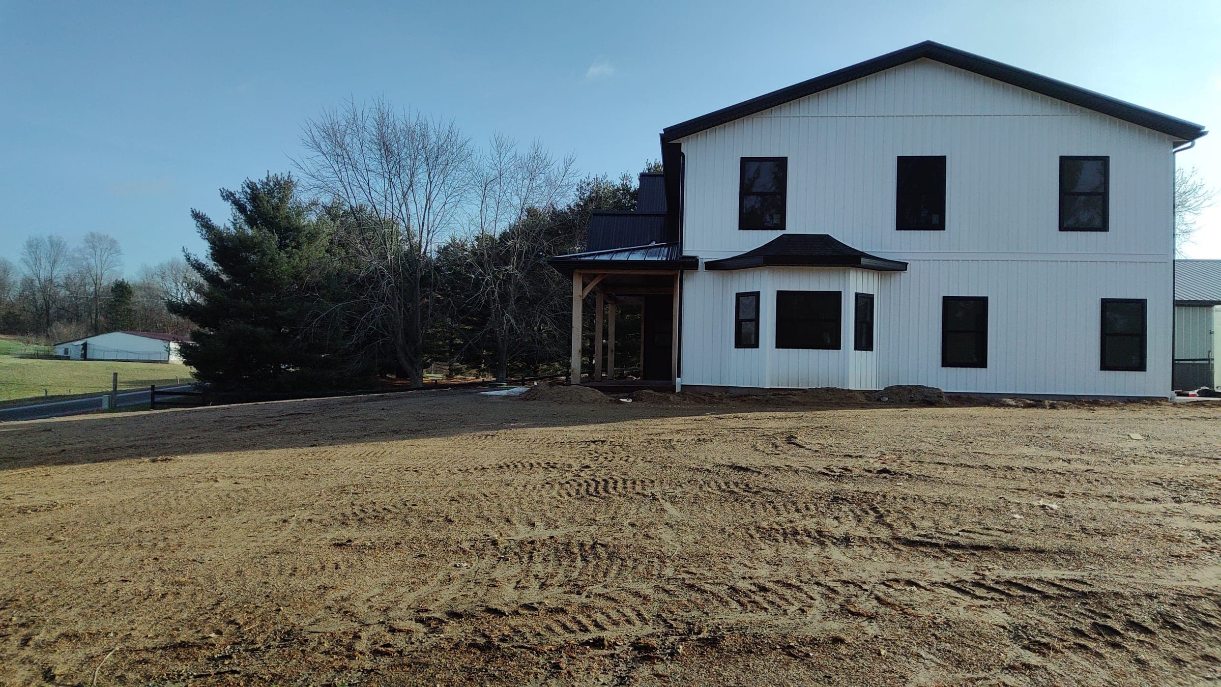 Rear view of two-story modern farmhouse with dark trim and graded yard