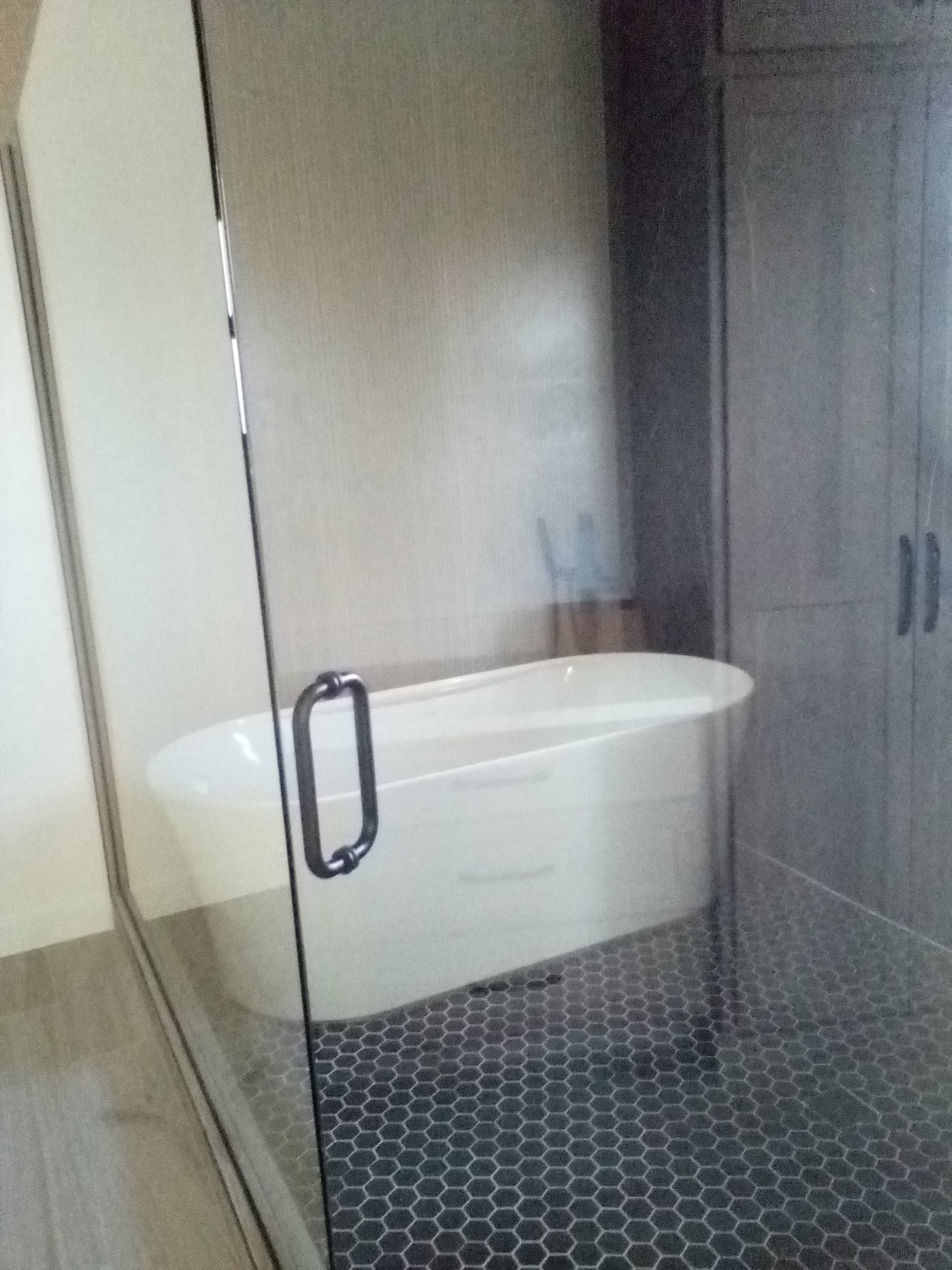 Freestanding soaking tub with black hexagon tile floor and glass enclosure in custom home